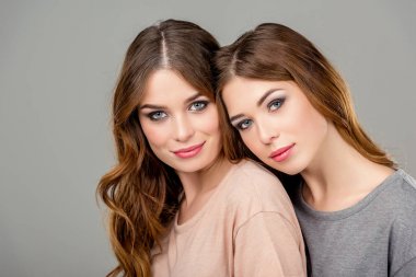 portrait of attractive twin sisters looking at camera isolated on grey clipart