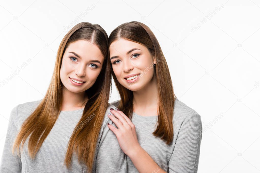 portrait of young smiling twins leaning on each other and looking at camera isolated on white