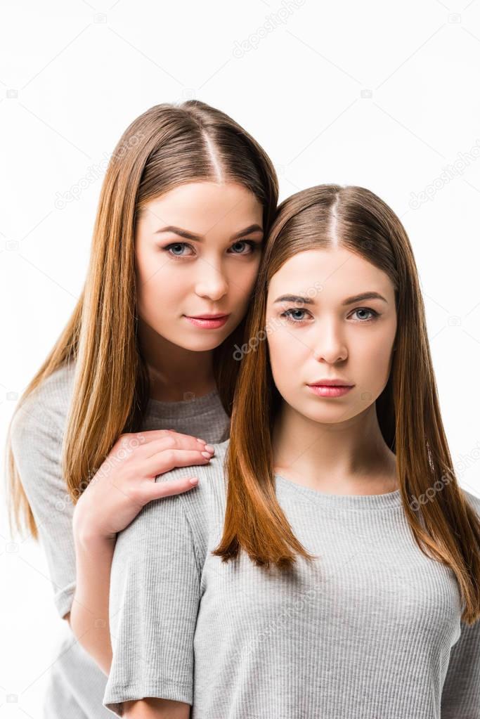 portrait of young pensive woman hugging twin sister isolated on white