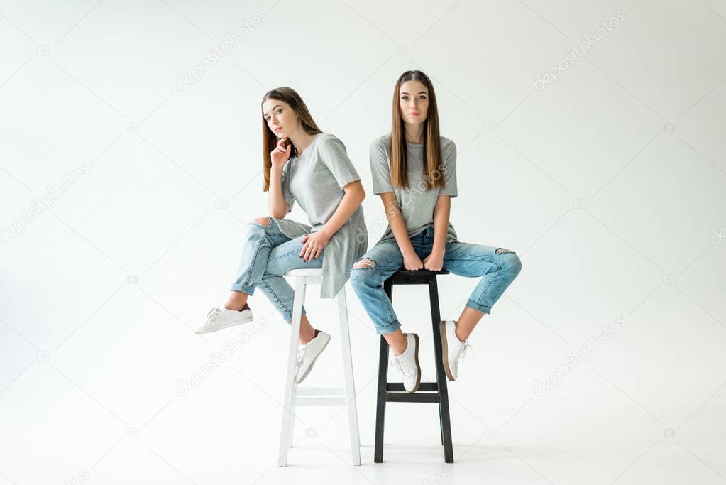 young twins in similar clothing looking at camera while sitting on chairs
