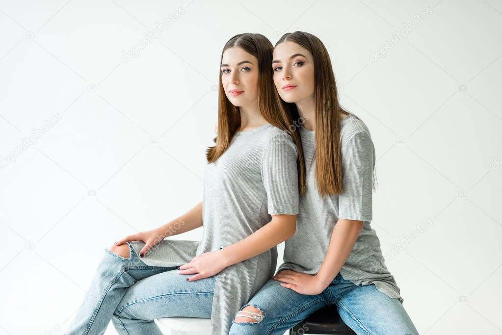 young twins in similar clothing looking at camera while sitting on chairs