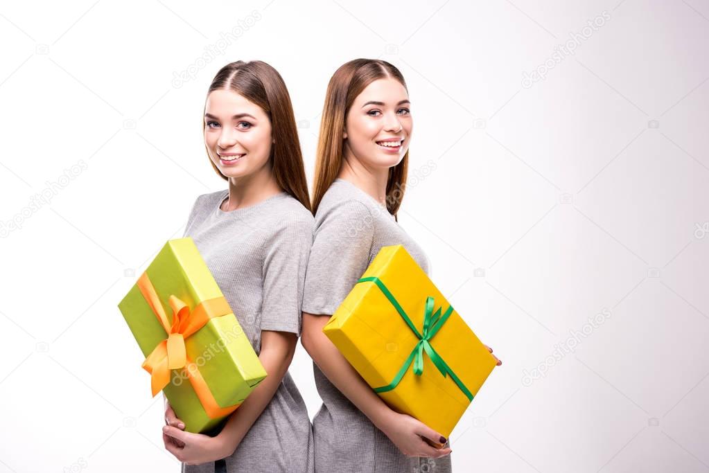 portrait of smiling twins with wrapped gifts in hands looking at camera