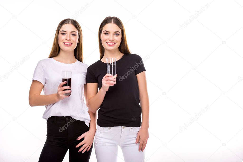 portrait of cheerful twins holding glasses of soda and water in hands isolated on white