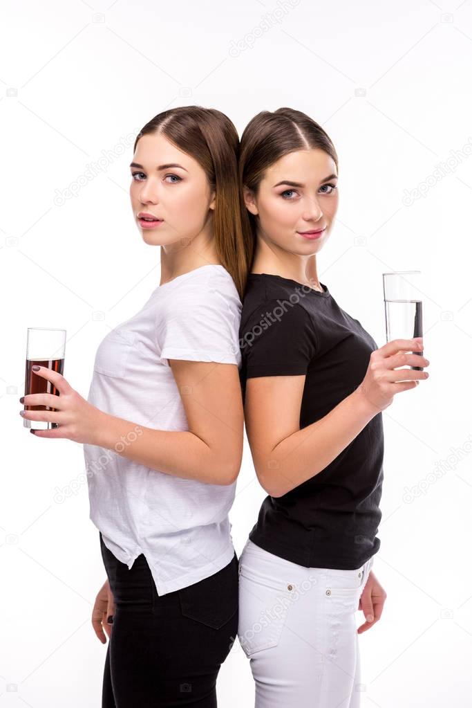 portrait of beautiful twins holding glasses of soda and water in hands isolated on white
