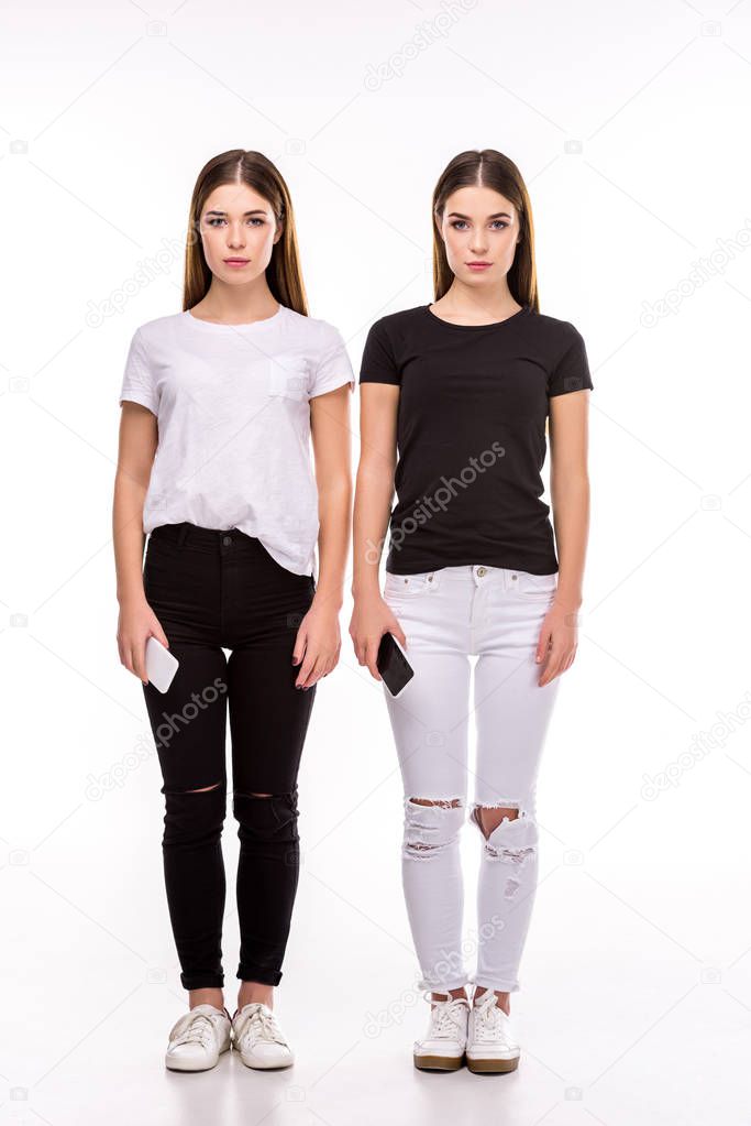 young twins with smartphones looking at camera isolated on white