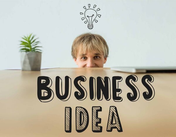 Man looking out from table and looking at camera with business idea inscription and light bulb icon