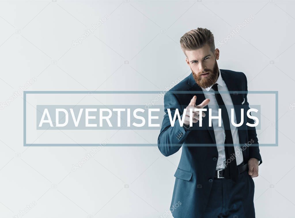 Handsome bearded businessman in stylish suit pointing at camera with finger. Business inscription on wall