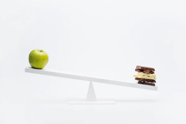 Apple and chocolate on seesaw — Stock Photo