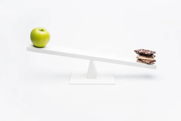 Apple and chocolate on seesaw — Stock Photo