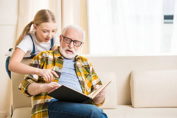 Abuelo con libro de lectura de chica - foto de stock