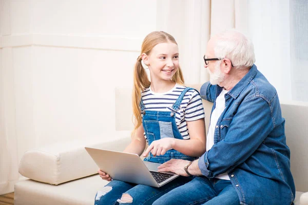 Chica con abuelo usando el ordenador portátil - foto de stock