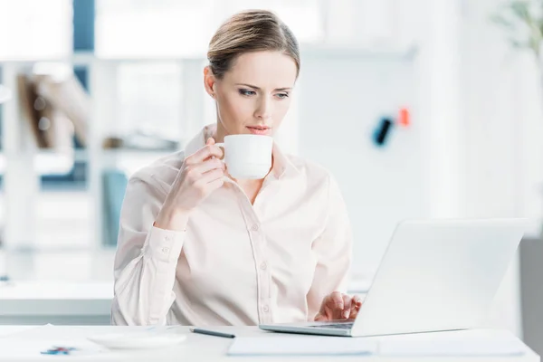 Бізнес-леді, що працює на ноутбуці та п'є каву — стокове фото