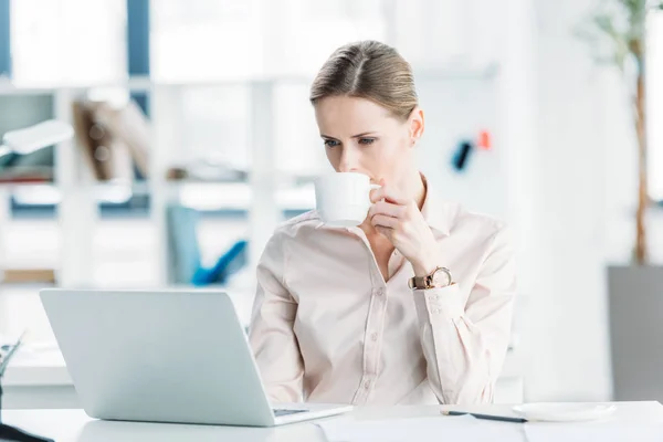 Businesswoman working on laptop and drinking coffee — Stock Photo