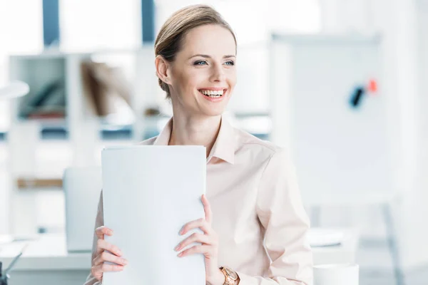 Sonriente mujer de negocios sosteniendo documentos en la oficina - foto de stock