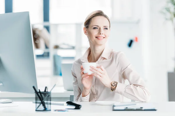 Улыбающаяся деловая женщина пьет кофе в офисе — стоковое фото