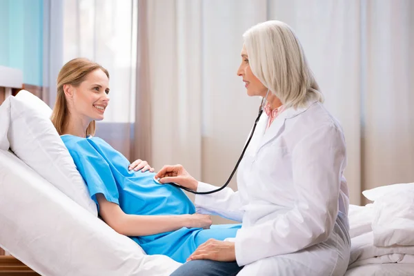 Médico escuchando vientre de la mujer embarazada - foto de stock