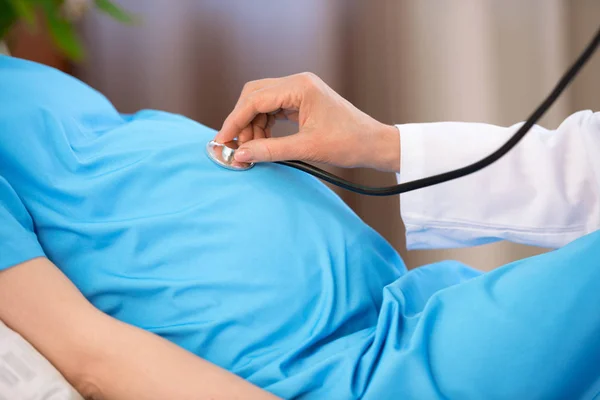 Médico escuchando vientre de la mujer embarazada - foto de stock