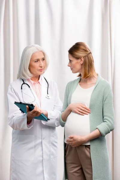 Médecin parlant avec une jeune femme enceinte — Photo de stock