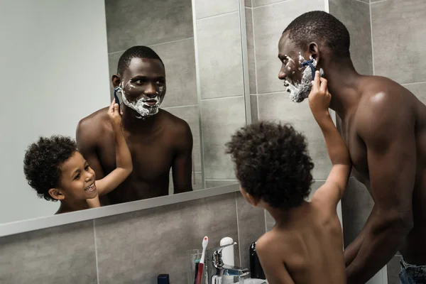 Lindo hijo afeitando su padre - foto de stock