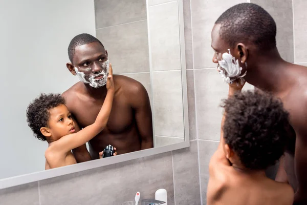Hijo aplicando espuma de afeitar en padre - foto de stock