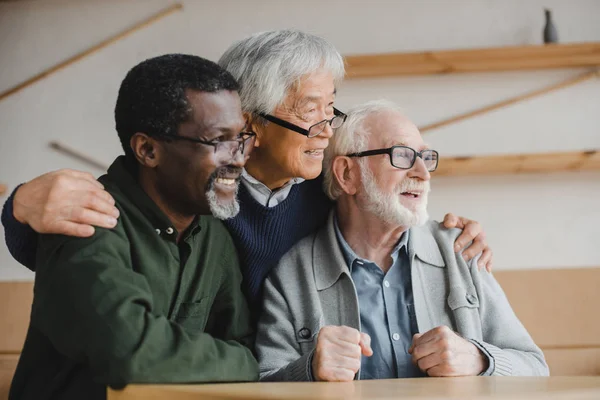 Amigos mayores abrazando y mirando hacia otro lado — Stock Photo