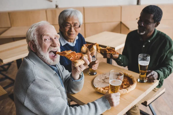 Amigos mayores bebiendo cerveza con pizza - foto de stock