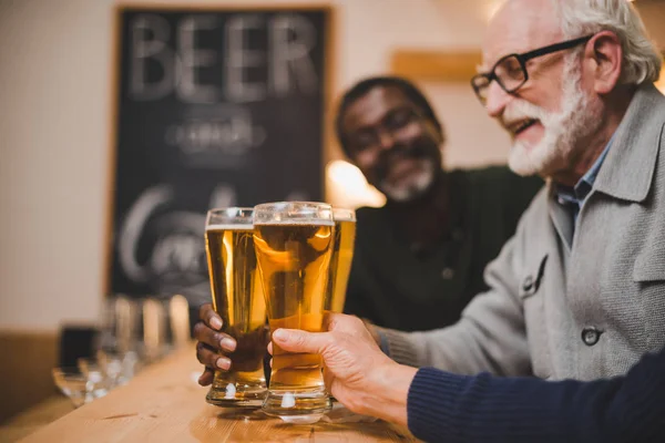 Amigos mayores tintineo vasos de cerveza - foto de stock