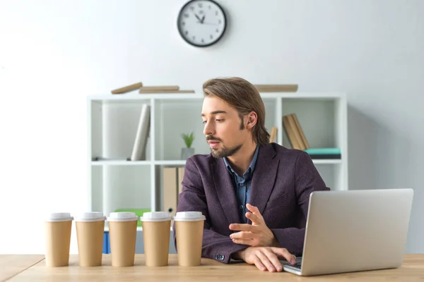 Businessman looking at disposable coffee cups — Stock Photo