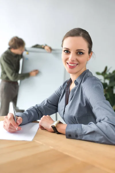 Mujer de negocios sonriente sentada a la mesa - foto de stock