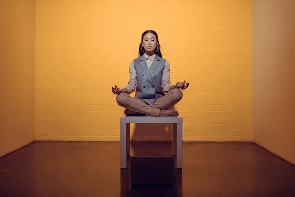 Asiatische Geschäftsfrau meditiert auf Tisch vor orangefarbener Wand — Stockfoto