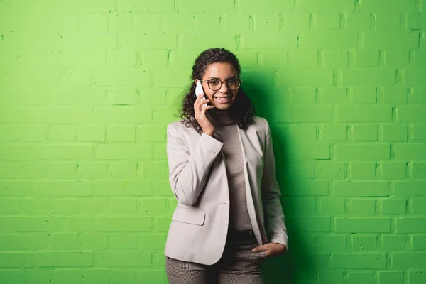 Mujer de negocios afroamericana hablando en teléfono inteligente frente a la pared verde - foto de stock