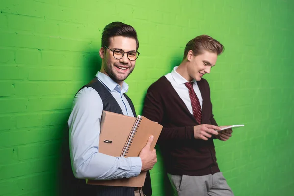 Young handsome businessmen with tablet and documents in front of green wall — Stock Photo