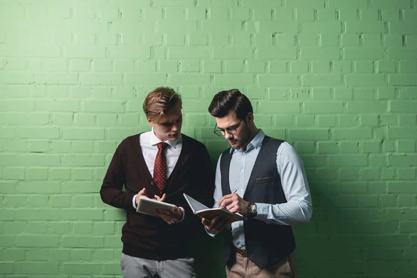 Jóvenes empresarios que trabajan con tableta digital y bloc de notas frente a la pared verde - foto de stock