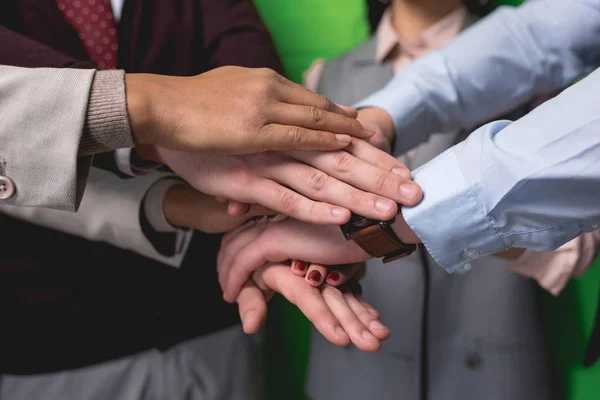 Обрезанный вид на бизнес-команды, держащихся за руки перед зеленой стеной — стоковое фото