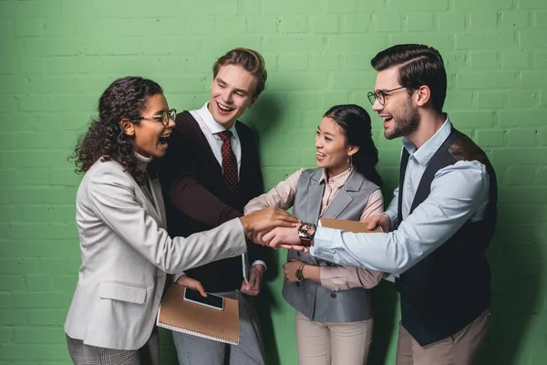 Team di lavoro multietnico eccitato che si tiene per mano insieme di fronte al muro verde — Foto stock