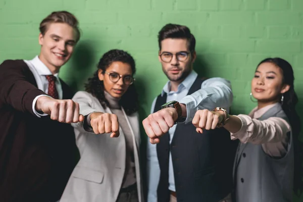 Empresarios multiculturales con puños frente a la pared verde - foto de stock