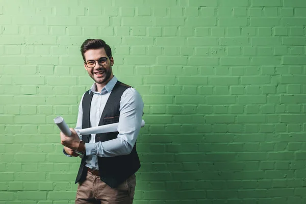 Young handsome businessman with blueprints in front of green wall — Stock Photo