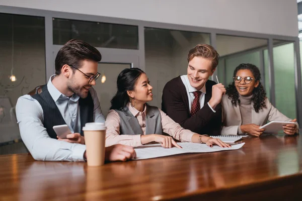 Team aziendale multietnico con caffè, dispositivi digitali e documenti che lavorano in ufficio — Foto stock