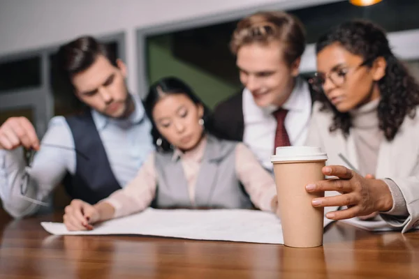 Enfoque selectivo del equipo empresarial multiétnico con café y documentos que trabajan en la oficina - foto de stock