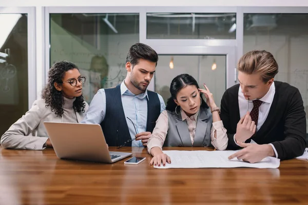 Empresarios multiculturales concentrados que trabajan con dispositivos digitales y documentos en la oficina - foto de stock