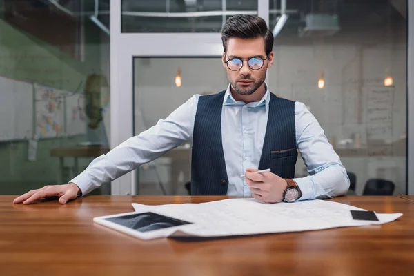 Homme d'affaires adulte dans les lunettes de travail avec le plan et les gadgets au bureau — Photo de stock