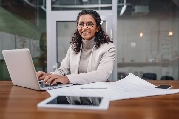 Afrikanisch-amerikanische Geschäftsfrau arbeitet mit Blaupause und Laptop im Büro — Stockfoto