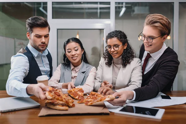 Sonrientes empresarios multiétnicos comiendo pizza en la oficina - foto de stock