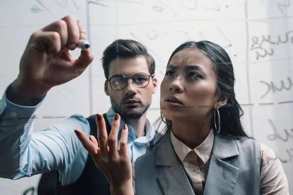 Hombre de negocios y mujer de negocios asiática escribiendo en tablero de cristal en la oficina - foto de stock