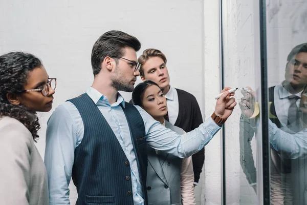 Multicultural businesspeople writing on glass board and working in office — Stock Photo