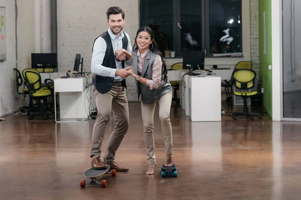Empresarios multiétnicos se divierten con patinetas en la oficina - foto de stock
