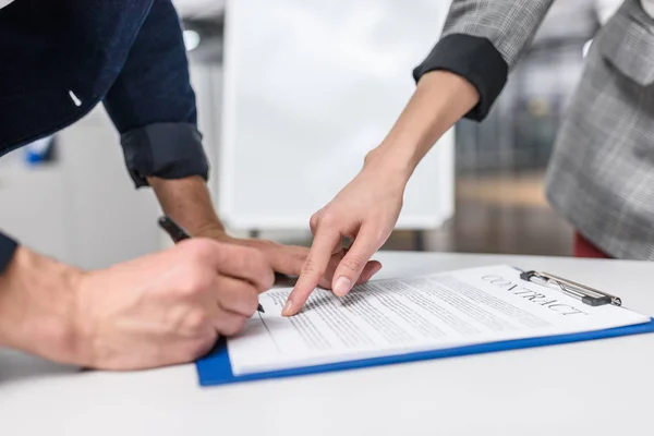 Крупным планом бизнесмен подписывает контракт, в то время как управляющая указывает на него — стоковое фото