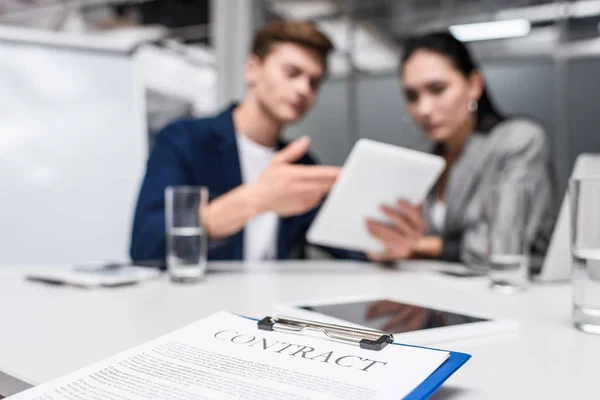 Geschäftsvertrag auf Klemmbrett im Büro mit Managern, die auf Tablet im Hintergrund schauen — Stockfoto