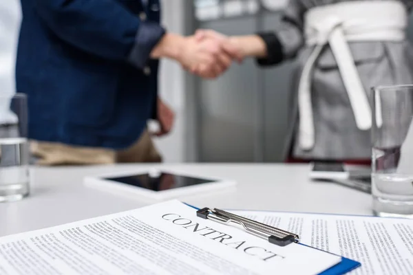 Business partners shaking hands with contract on table on foreground — Stock Photo