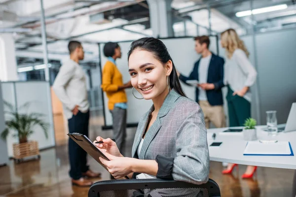 Jeune belle femme d'affaires écriture sur presse-papiers au bureau moderne — Photo de stock